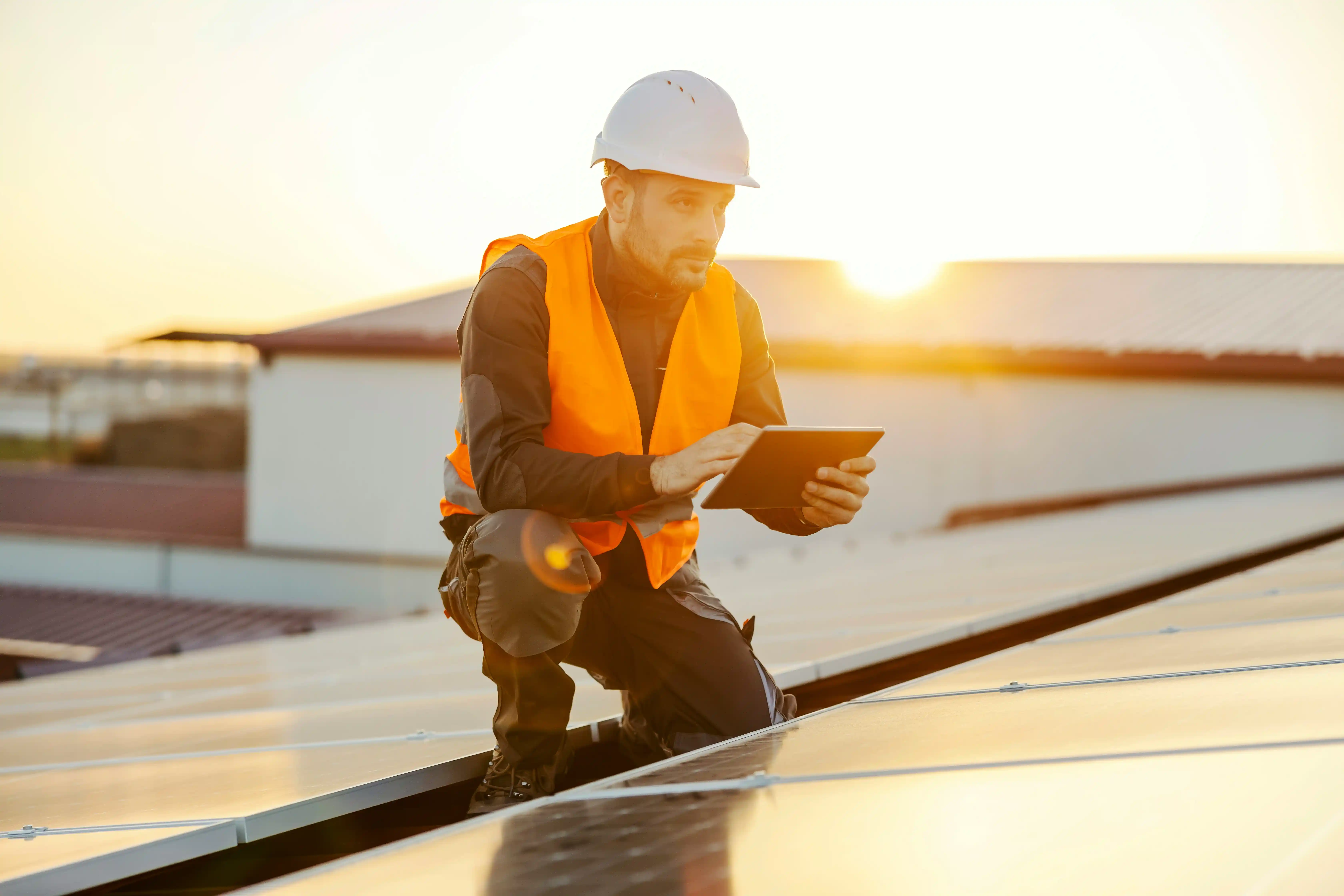 Handwerker sitzt auf Dach und bedient Tablet